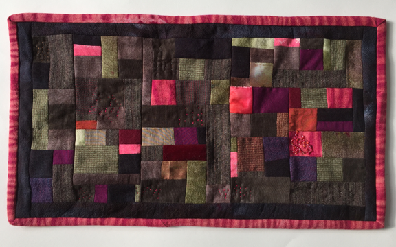 horizontally oriented pieced quilt with squares in tree colors and textures with beaded flame