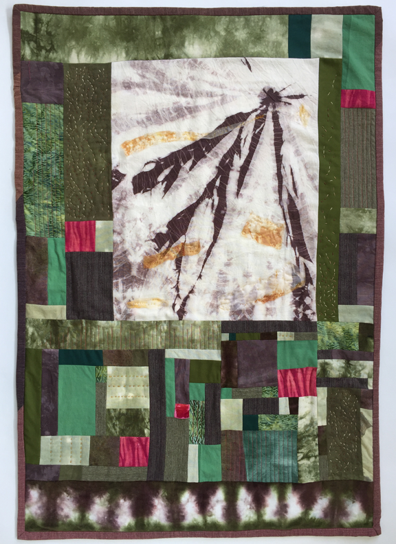 vertically oriented pieced quilt with squares in tree colors and textures with central larger rectangle of radial lines and patches like haze
