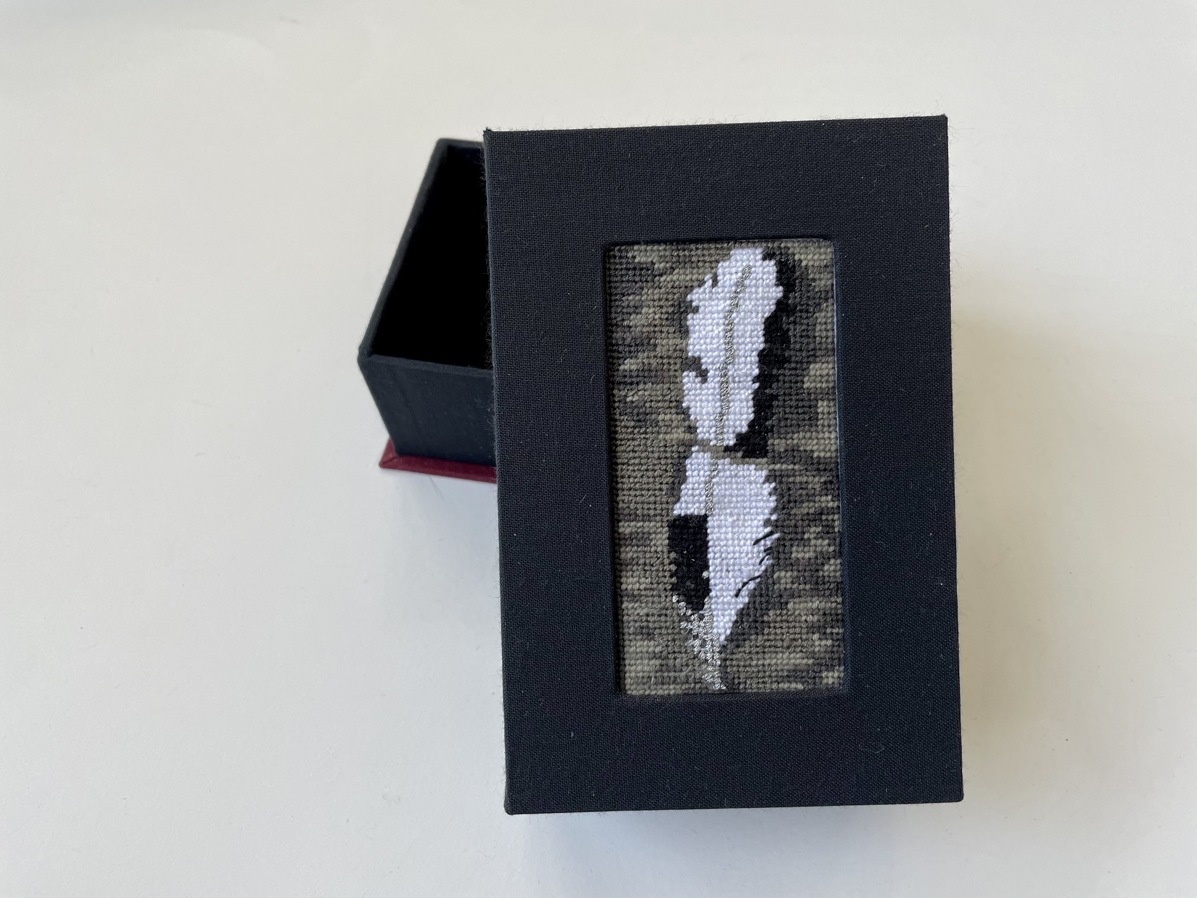 a box with an inset needlepoint of one feather